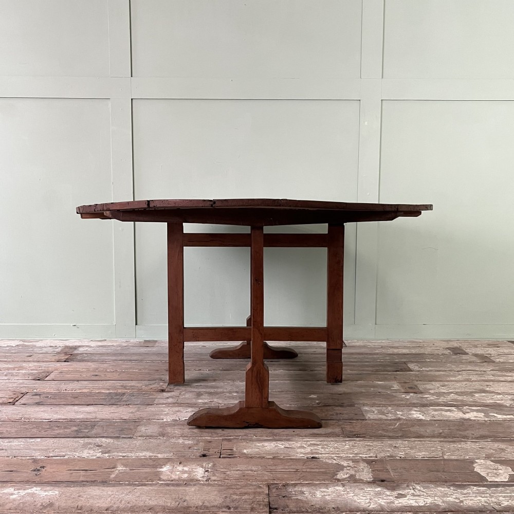 A 19th-century French circular tilt-top vendange table constructed from warm brown planked timber, shown tilted upright against a pale green wall. View VIII