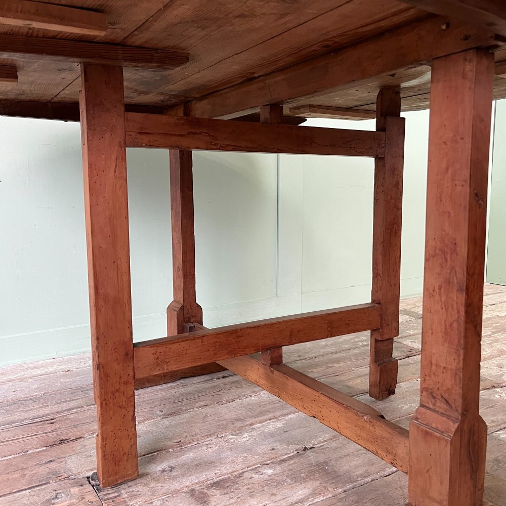 A 19th-century French circular tilt-top vendange table constructed from warm brown planked timber, shown tilted upright against a pale green wall. View X