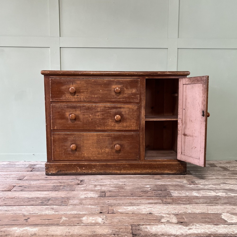 An antique Victorian warm brown pine cupboard featuring three drawers on the left with turned wooden knobs alongside a single panelled door on the right. View II