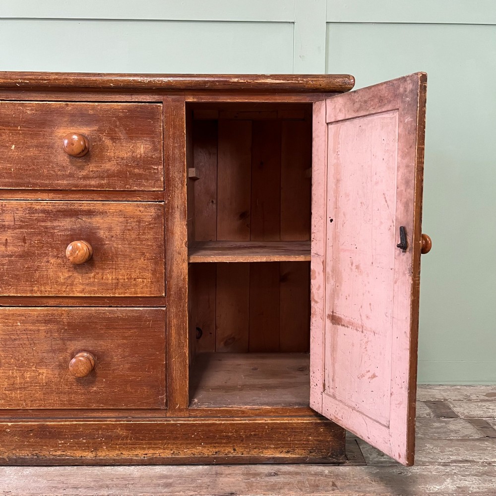 An antique Victorian warm brown pine cupboard featuring three drawers on the left with turned wooden knobs alongside a single panelled door on the right. View III