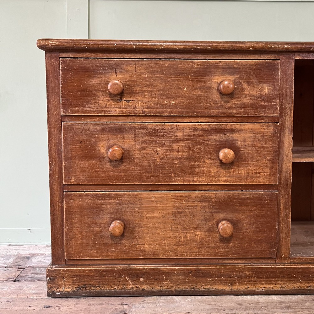 An antique Victorian warm brown pine cupboard featuring three drawers on the left with turned wooden knobs alongside a single panelled door on the right. View IV