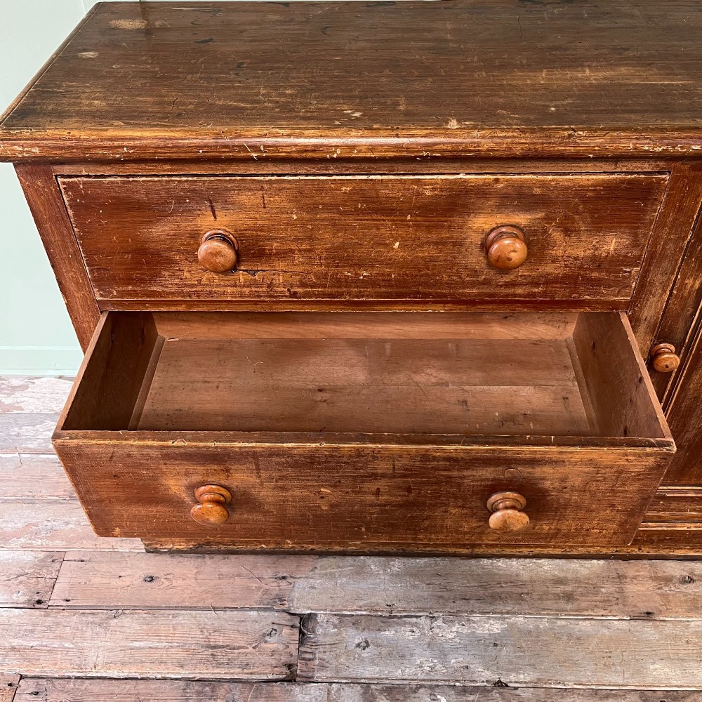 An antique Victorian warm brown pine cupboard featuring three drawers on the left with turned wooden knobs alongside a single panelled door on the right. View V