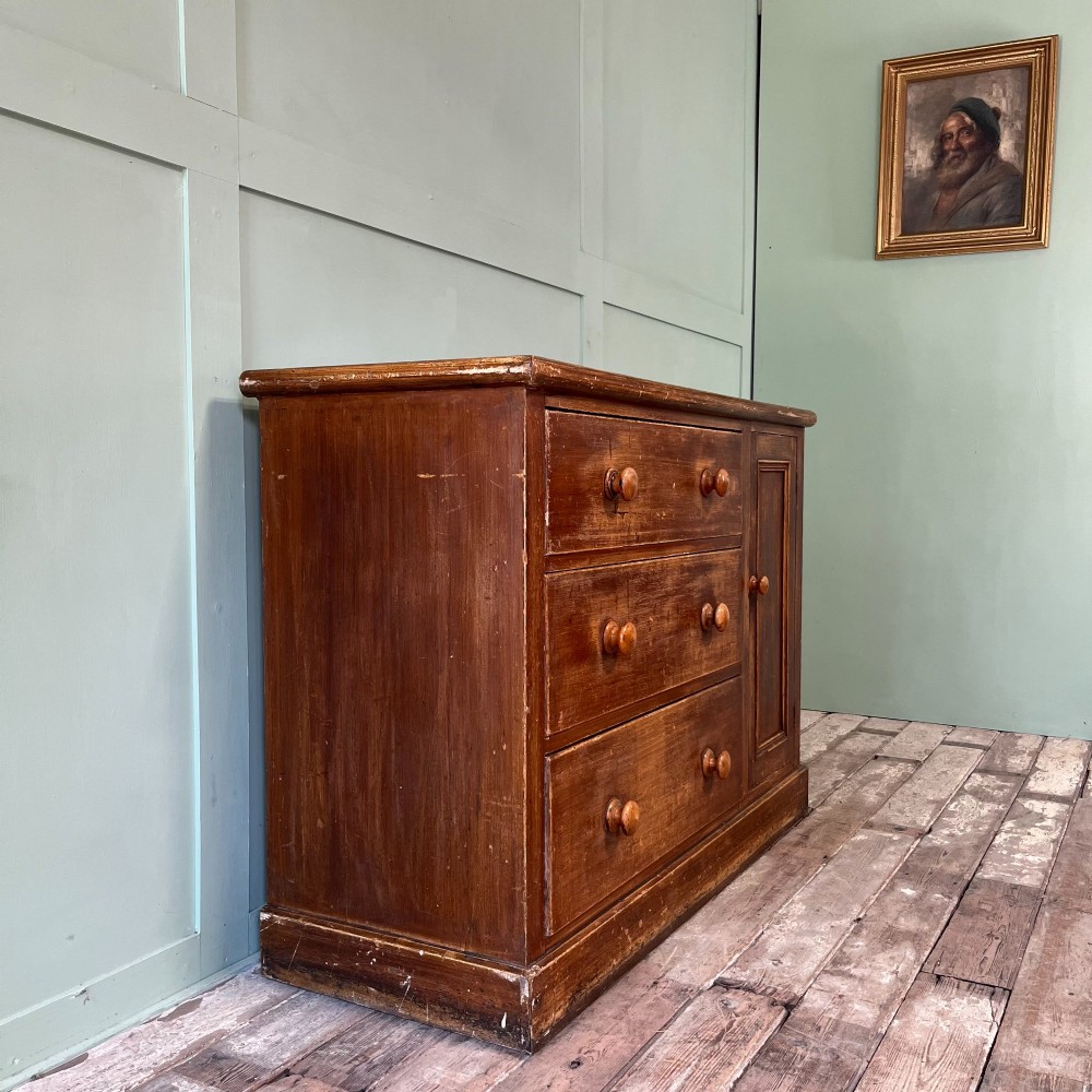An antique Victorian warm brown pine cupboard featuring three drawers on the left with turned wooden knobs alongside a single panelled door on the right. View VI