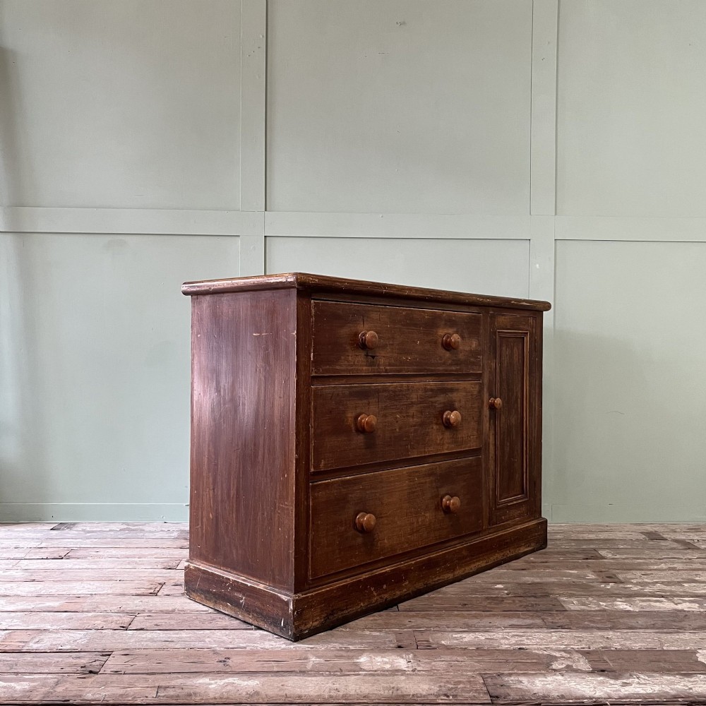 An antique Victorian warm brown pine cupboard featuring three drawers on the left with turned wooden knobs alongside a single panelled door on the right. View XII