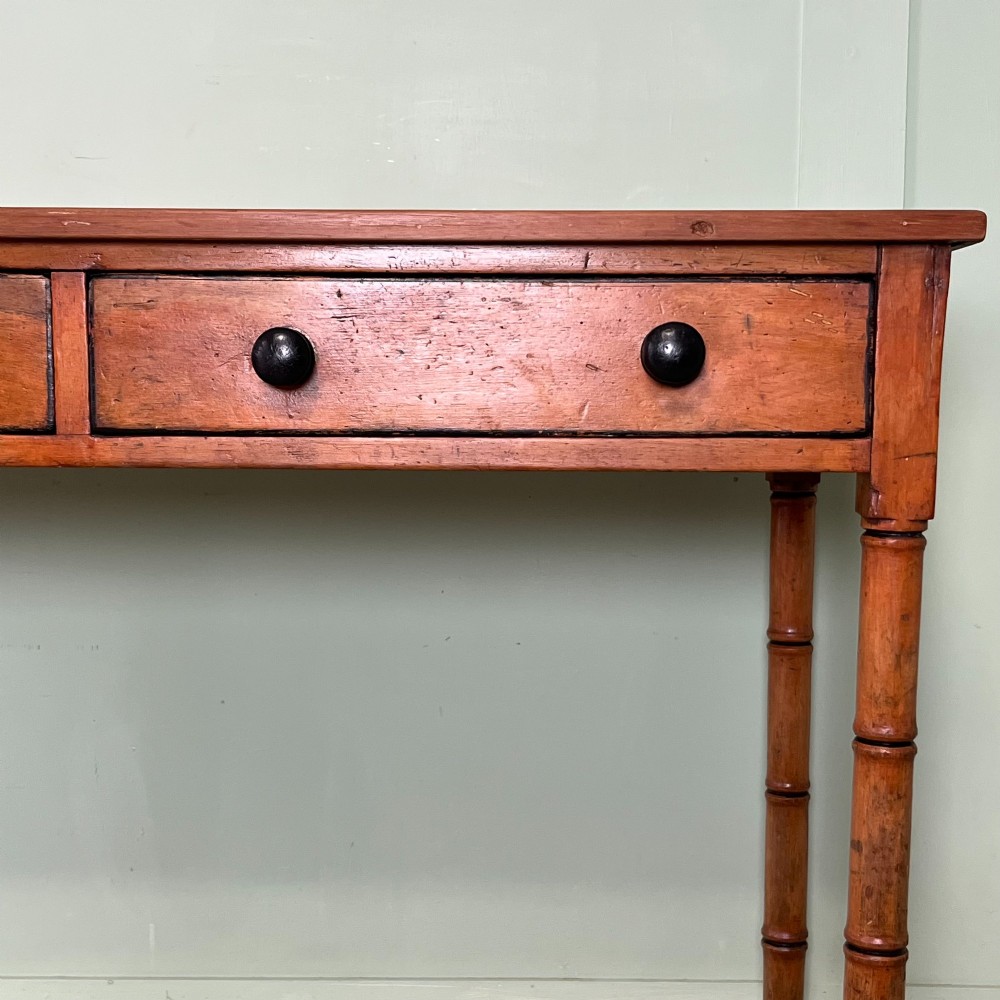 An antique pine hall table featuring two drawers with dark turned handles and slender turned legs. View V