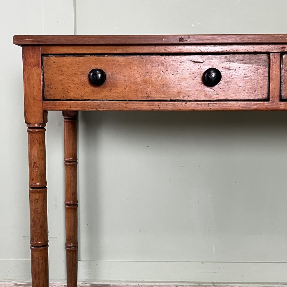 An antique pine hall table featuring two drawers with dark turned handles and slender turned legs. View VI
