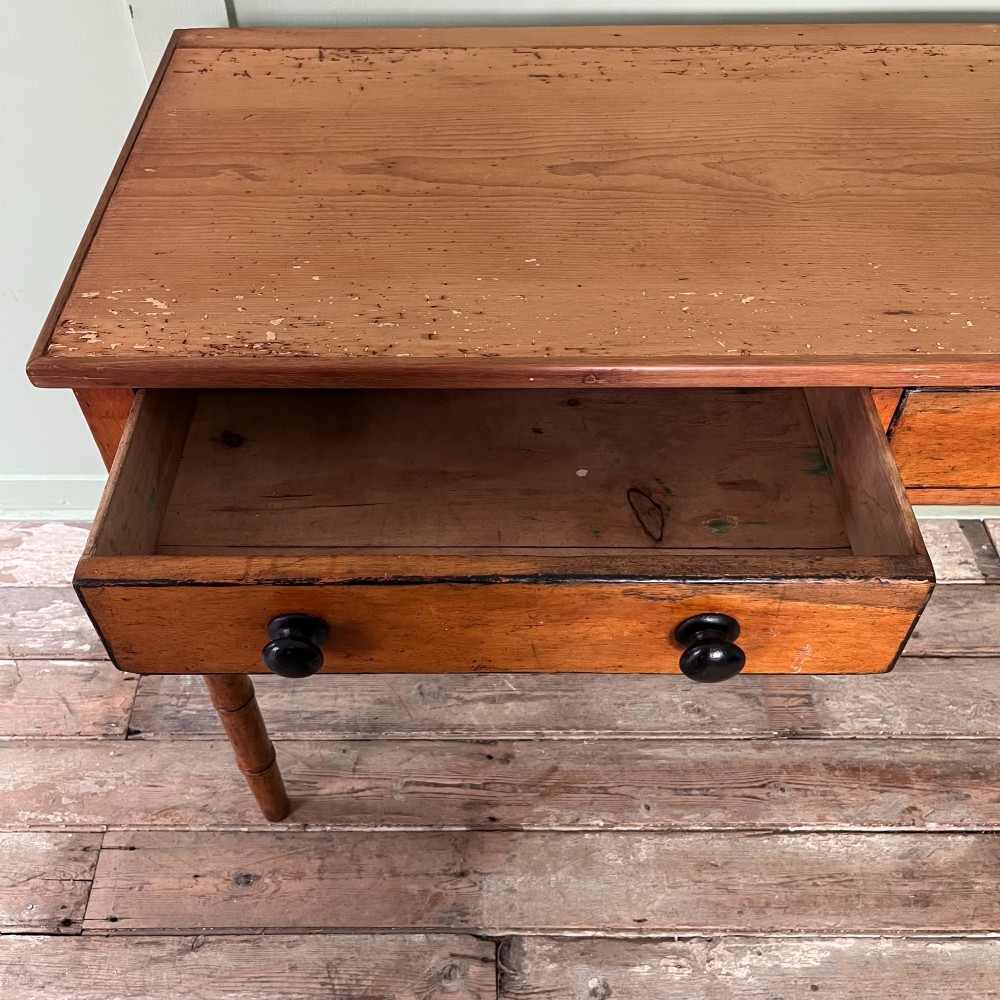 An antique pine hall table featuring two drawers with dark turned handles and slender turned legs. View VII