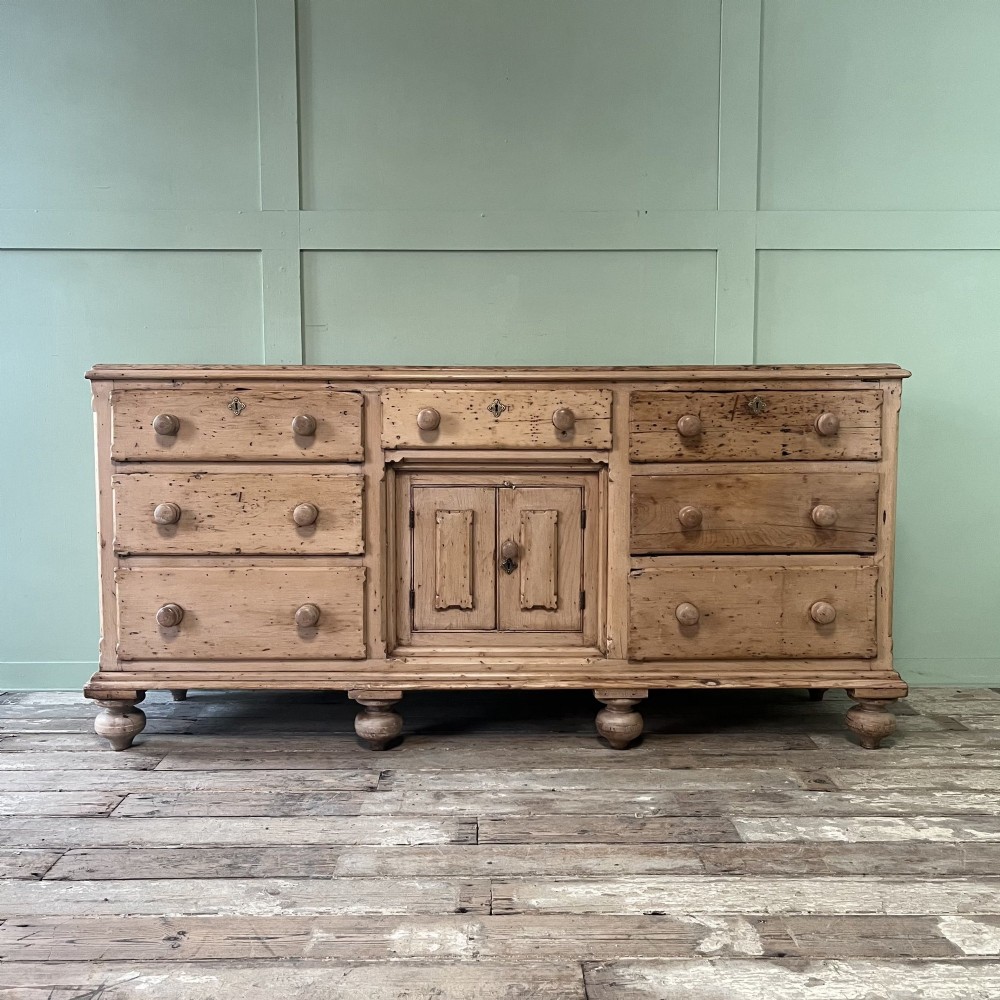 A long Georgian pine sideboard featuring six side drawers flanking a central top drawer and small double-door cupboard, supported by turned bun feet.