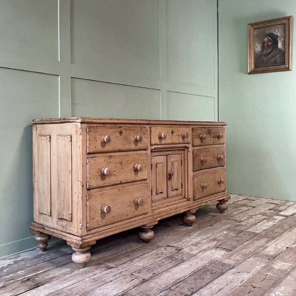 A long Georgian pine sideboard featuring six side drawers flanking a central top drawer and small double-door cupboard, supported by turned bun feet. View II