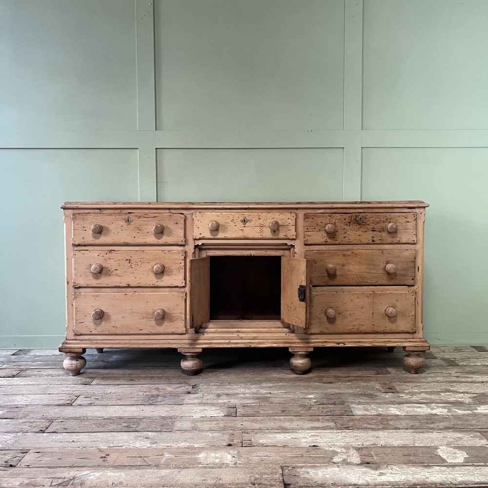 A long Georgian pine sideboard featuring six side drawers flanking a central top drawer and small double-door cupboard, supported by turned bun feet. View III
