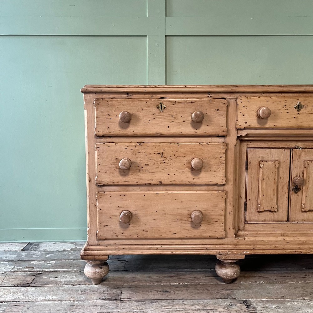 A long Georgian pine sideboard featuring six side drawers flanking a central top drawer and small double-door cupboard, supported by turned bun feet. View IV