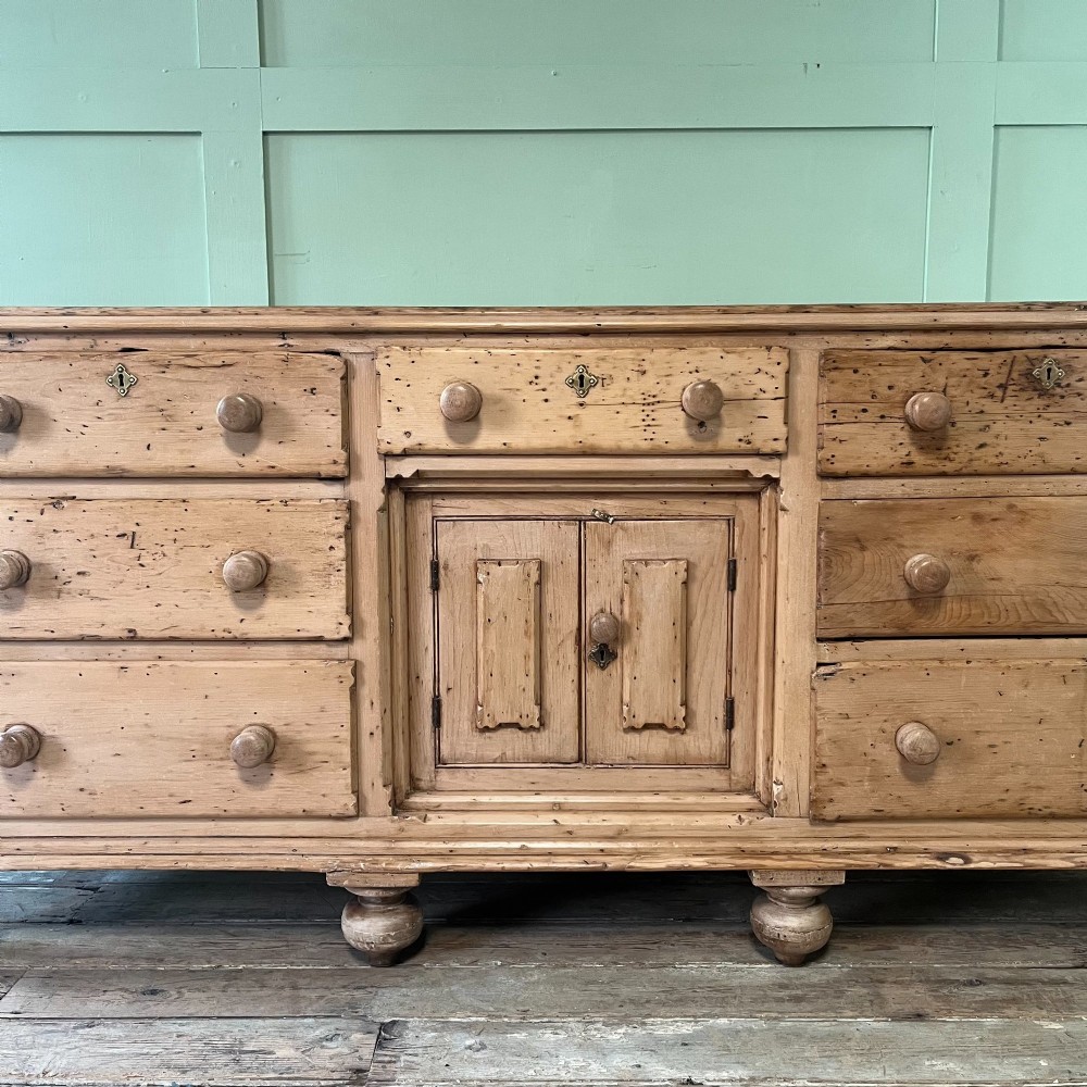 A long Georgian pine sideboard featuring six side drawers flanking a central top drawer and small double-door cupboard, supported by turned bun feet. View V