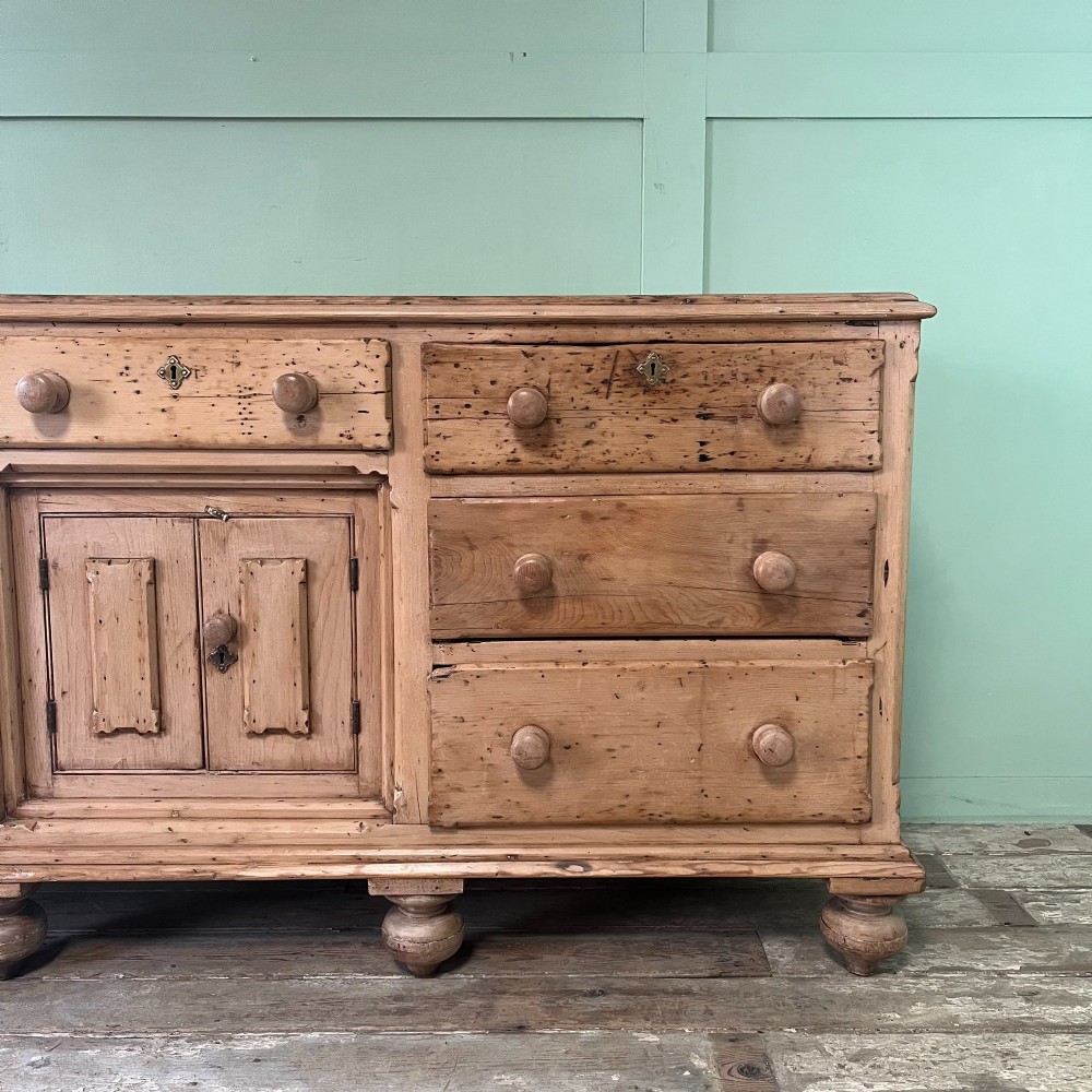 A long Georgian pine sideboard featuring six side drawers flanking a central top drawer and small double-door cupboard, supported by turned bun feet. View VI