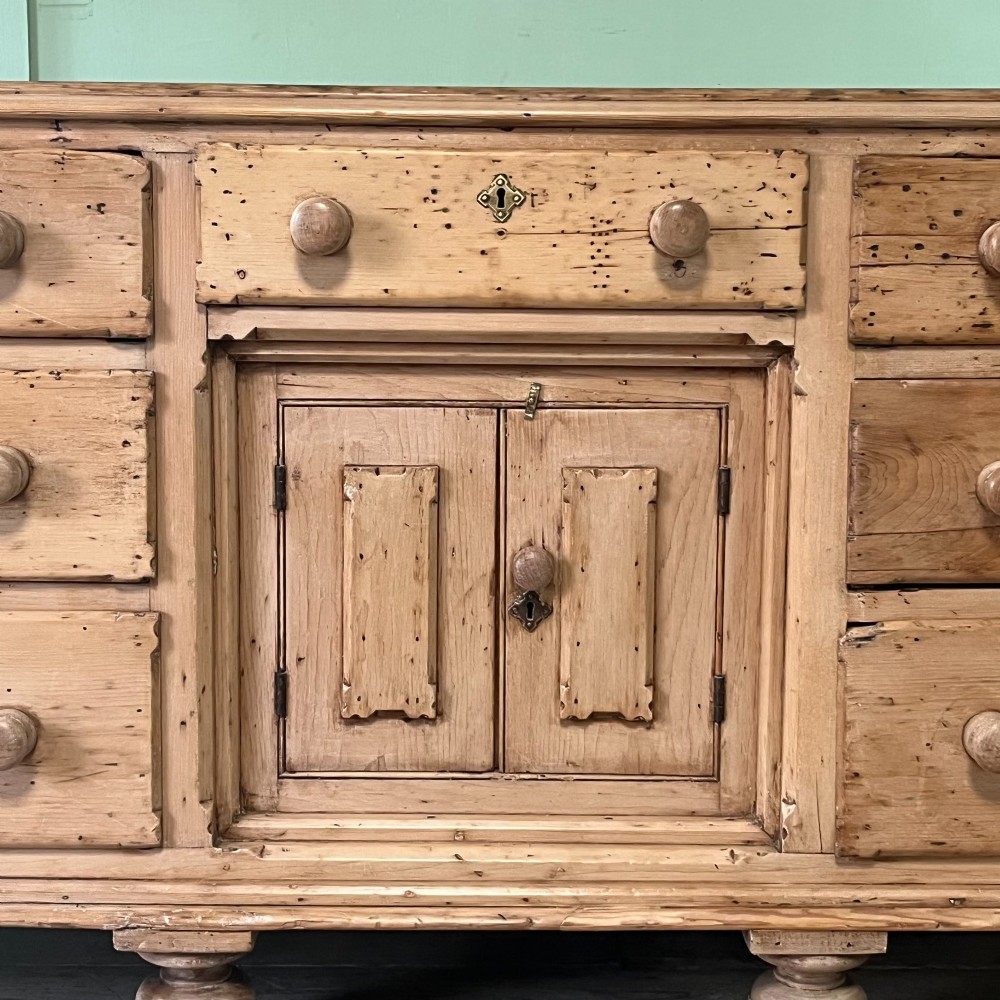 A long Georgian pine sideboard featuring six side drawers flanking a central top drawer and small double-door cupboard, supported by turned bun feet. View VII