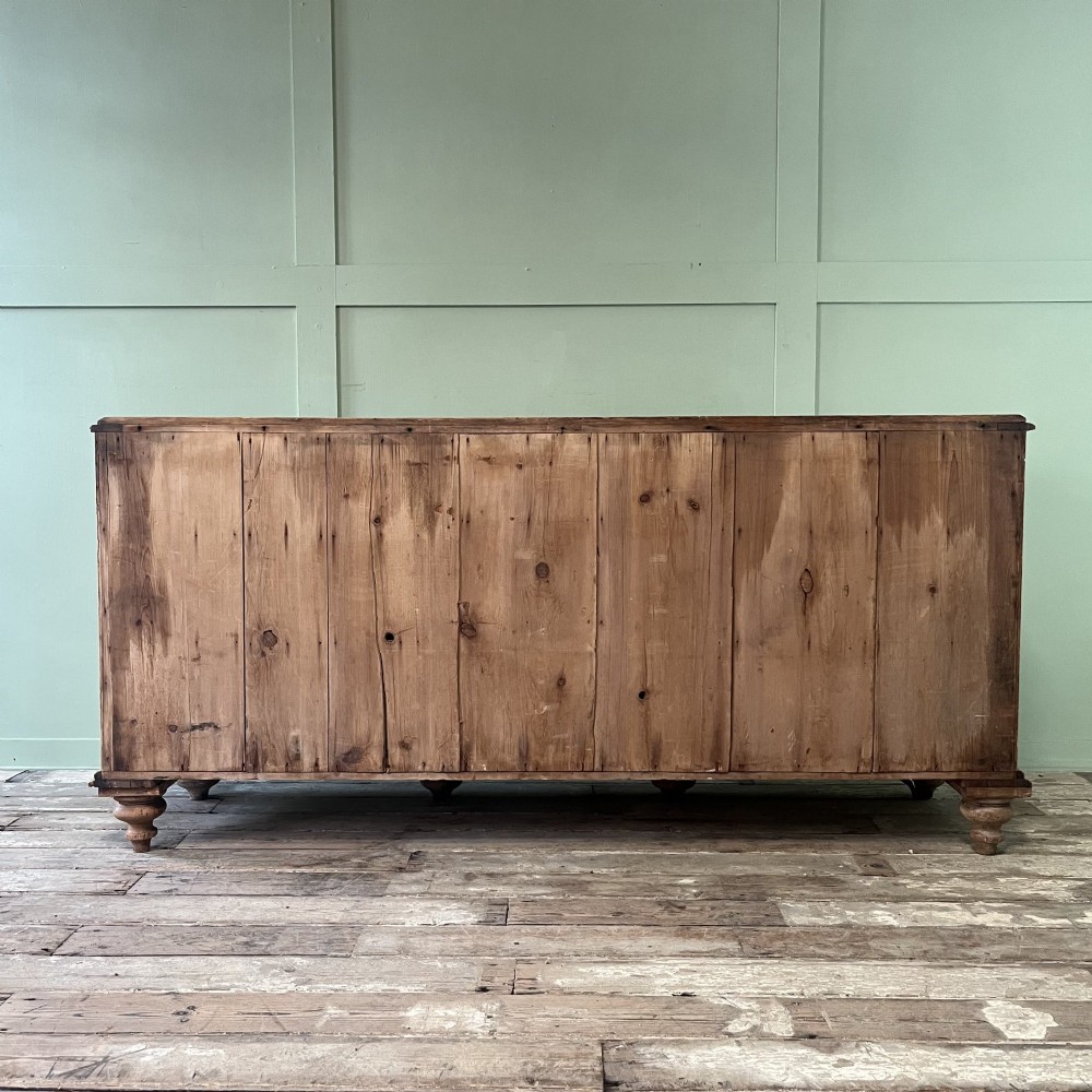 A long Georgian pine sideboard featuring six side drawers flanking a central top drawer and small double-door cupboard, supported by turned bun feet. View XII