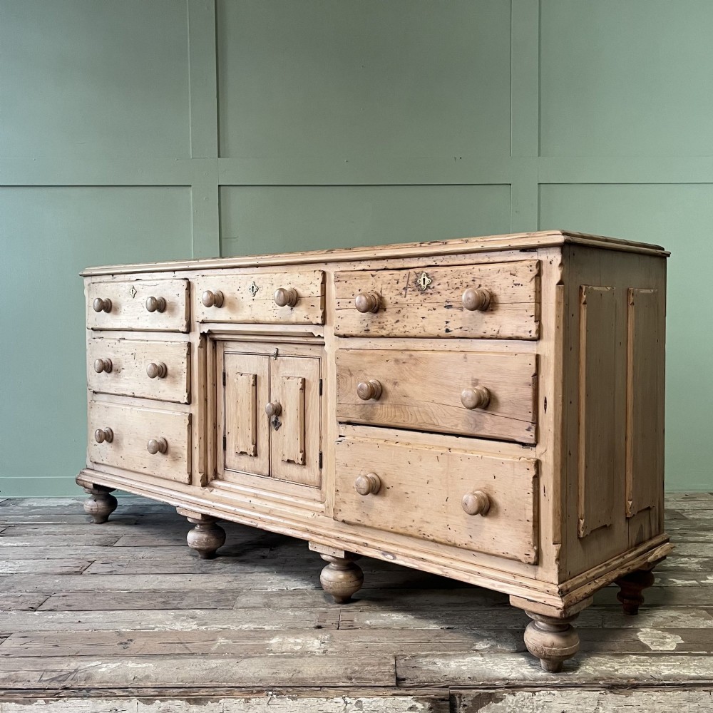 A long Georgian pine sideboard featuring six side drawers flanking a central top drawer and small double-door cupboard, supported by turned bun feet. View XIV