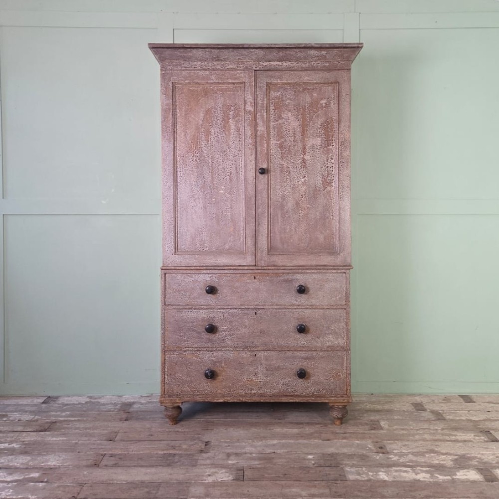 A tall late Georgian painted pine housekeepers cupboard featuring panelled upper doors and three lower drawers on turned feet.