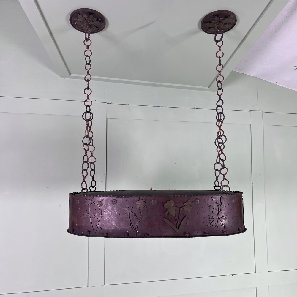 An oval Arts and Crafts copper pendant light featuring hand-chased floral motifs suspended from twin copper link chains with ceiling roses.