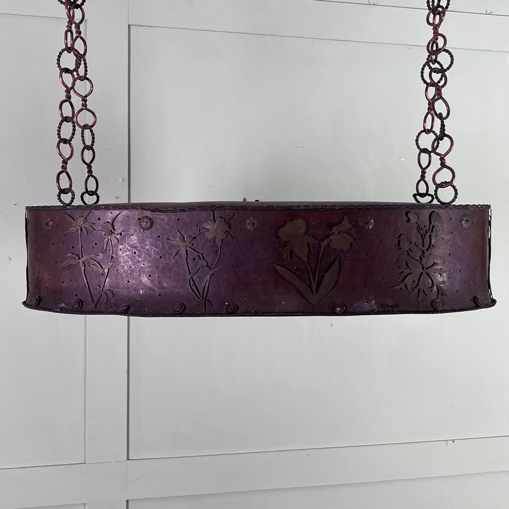 An oval Arts and Crafts copper pendant light featuring hand-chased floral motifs suspended from twin copper link chains with ceiling roses. View II