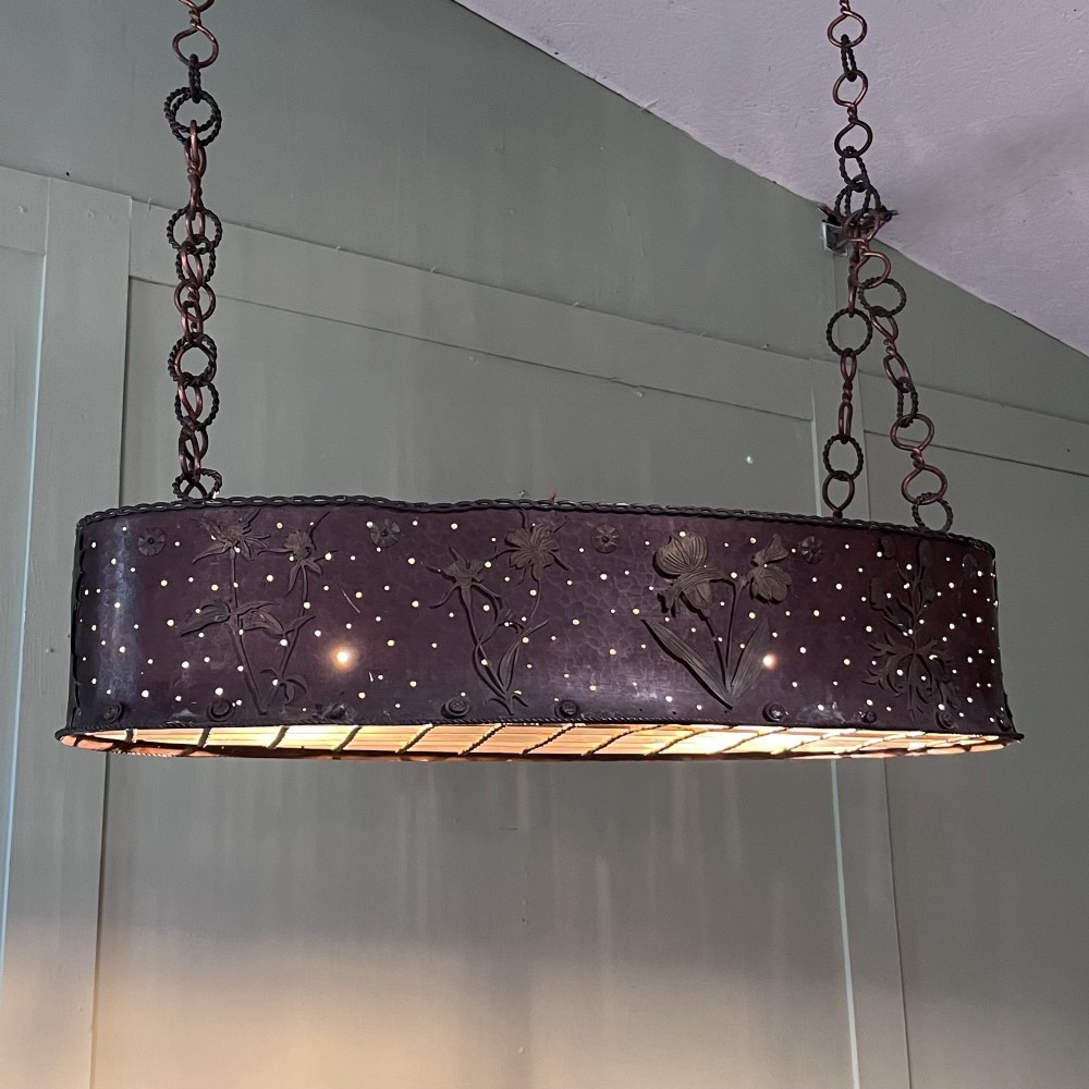 An oval Arts and Crafts copper pendant light featuring hand-chased floral motifs suspended from twin copper link chains with ceiling roses. View III