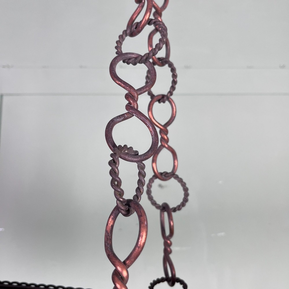An oval Arts and Crafts copper pendant light featuring hand-chased floral motifs suspended from twin copper link chains with ceiling roses. View X