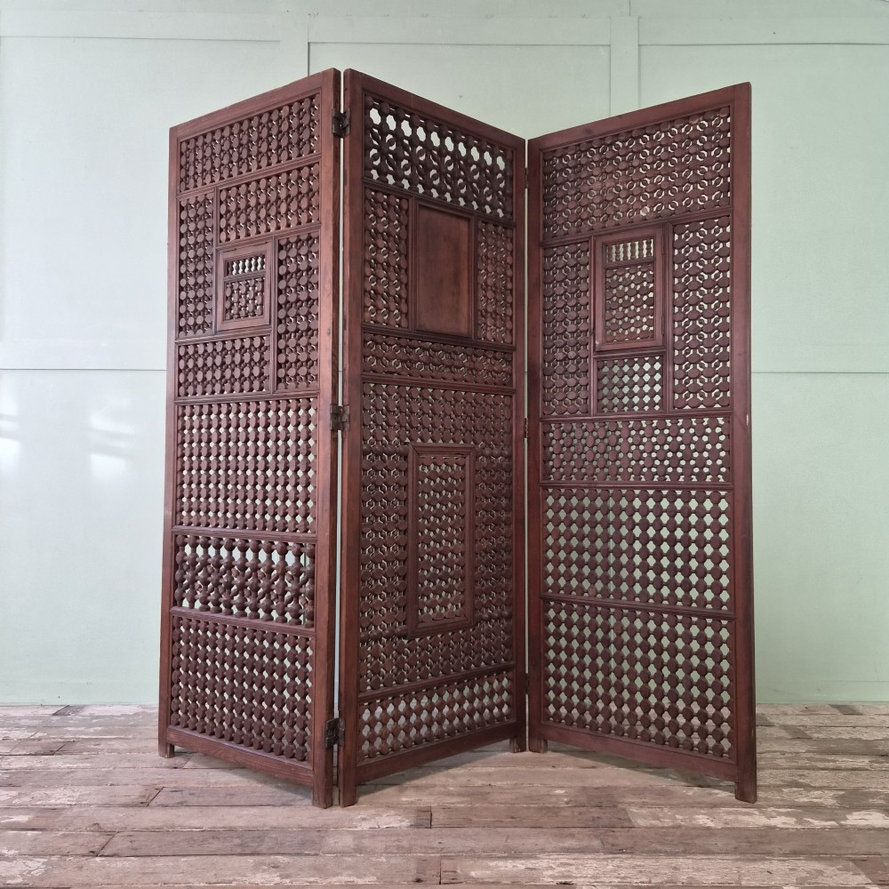 A three-panel antique wooden folding screen featuring intricate turned spindle lattice work and geometric carved panels in a dark brown finish.
