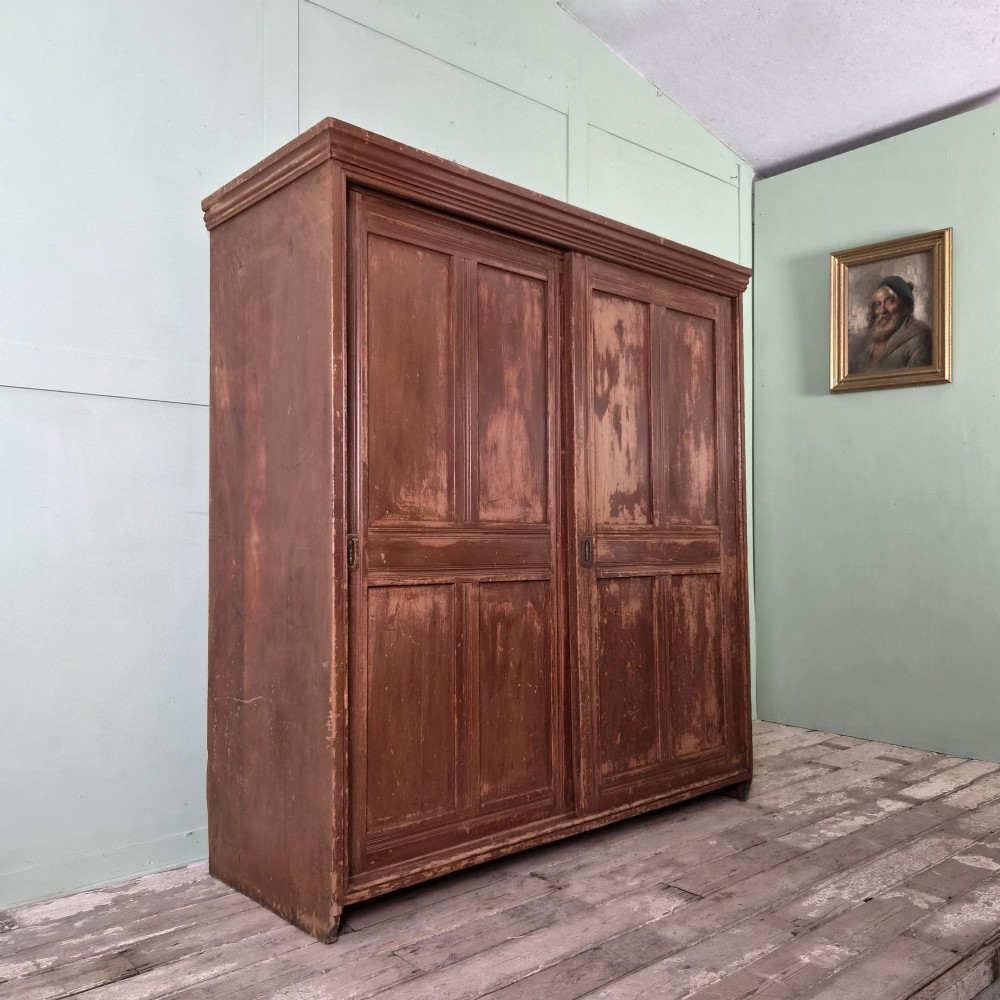 A large 19th-century pine freestanding cupboard featuring two sliding panel doors with an aged reddish-brown patinated finish and a moulded top cornice.