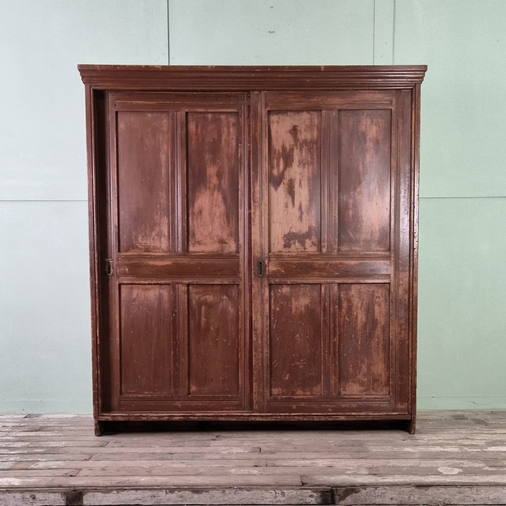 A large 19th-century pine freestanding cupboard featuring two sliding panel doors with an aged reddish-brown patinated finish and a moulded top cornice. View II