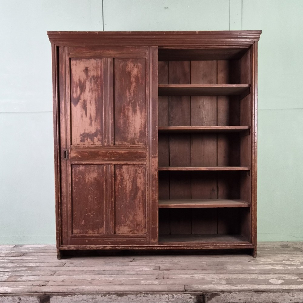 A large 19th-century pine freestanding cupboard featuring two sliding panel doors with an aged reddish-brown patinated finish and a moulded top cornice. View V