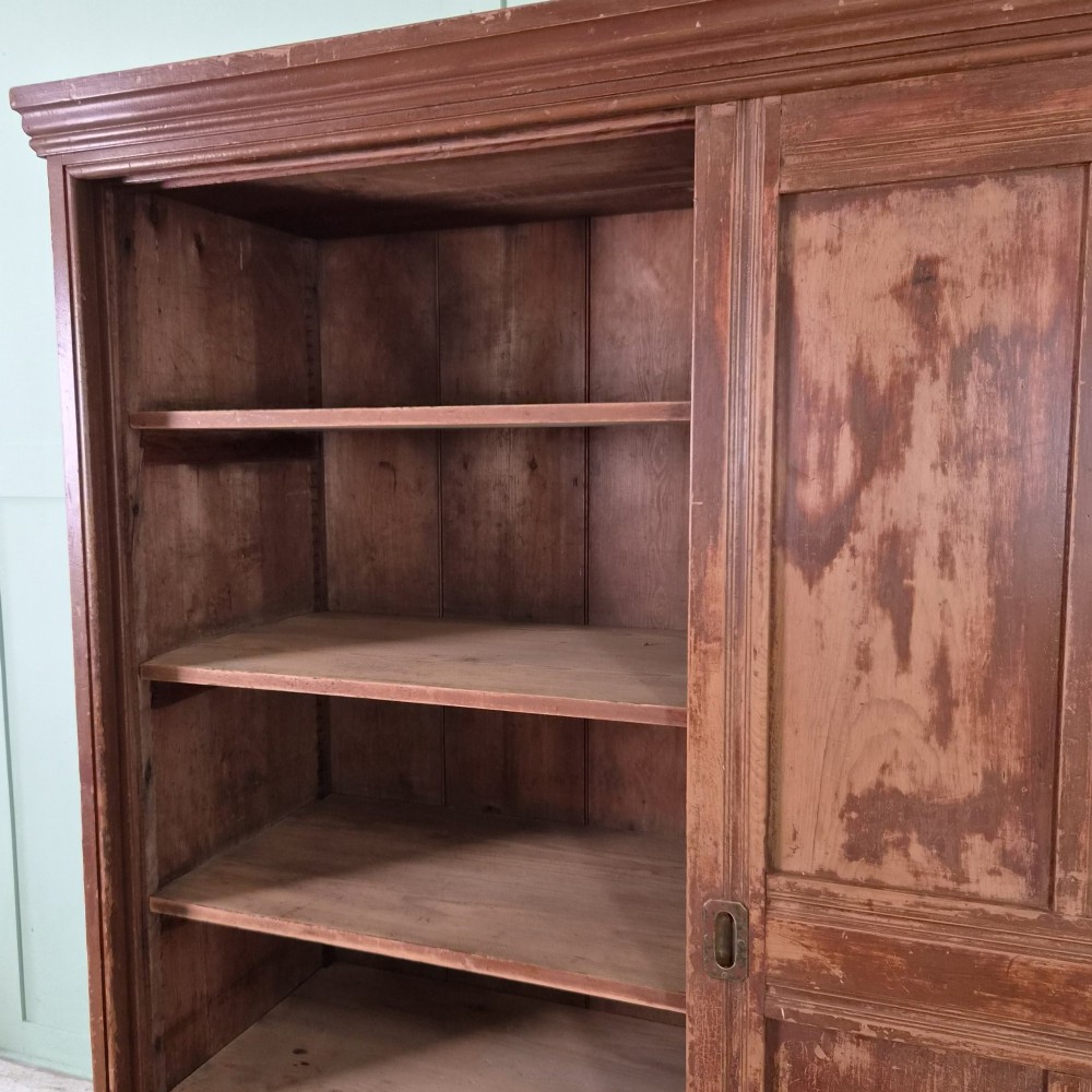 A large 19th-century pine freestanding cupboard featuring two sliding panel doors with an aged reddish-brown patinated finish and a moulded top cornice. View IX