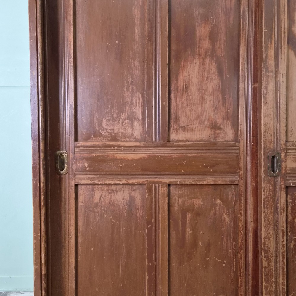 A large 19th-century pine freestanding cupboard featuring two sliding panel doors with an aged reddish-brown patinated finish and a moulded top cornice. View XII