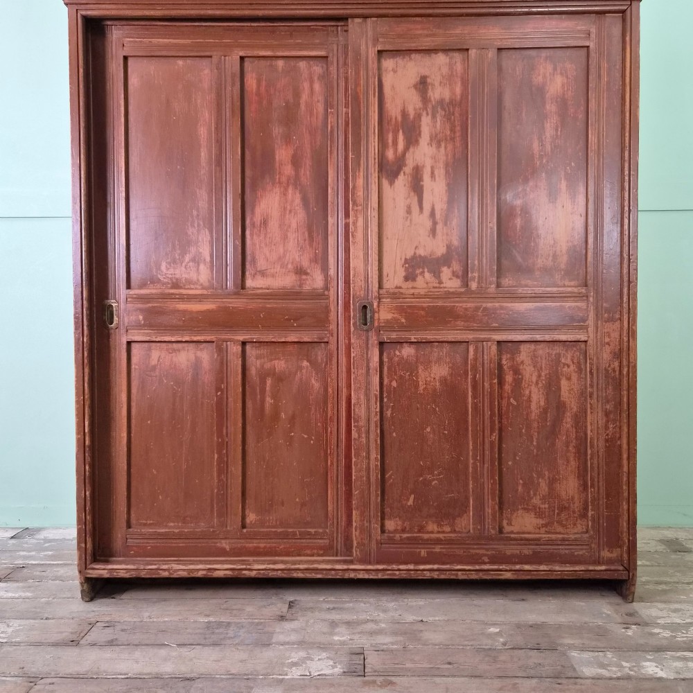 A large 19th-century pine freestanding cupboard featuring two sliding panel doors with an aged reddish-brown patinated finish and a moulded top cornice. View XIII