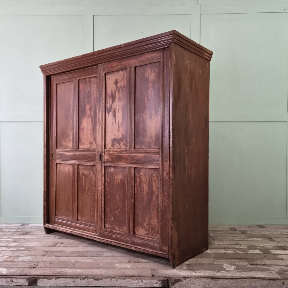 A large 19th-century pine freestanding cupboard featuring two sliding panel doors with an aged reddish-brown patinated finish and a moulded top cornice. View XIV