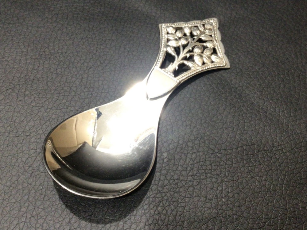A sterling silver tea caddy spoon featuring a pierced diamond-shaped handle decorated with a tree of life motif and a polished pear-shaped bowl. View II