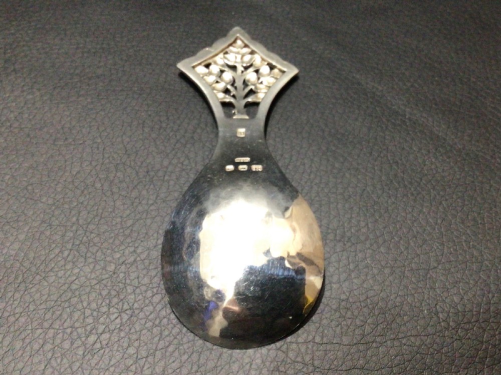 A sterling silver tea caddy spoon featuring a pierced diamond-shaped handle decorated with a tree of life motif and a polished pear-shaped bowl. View IV