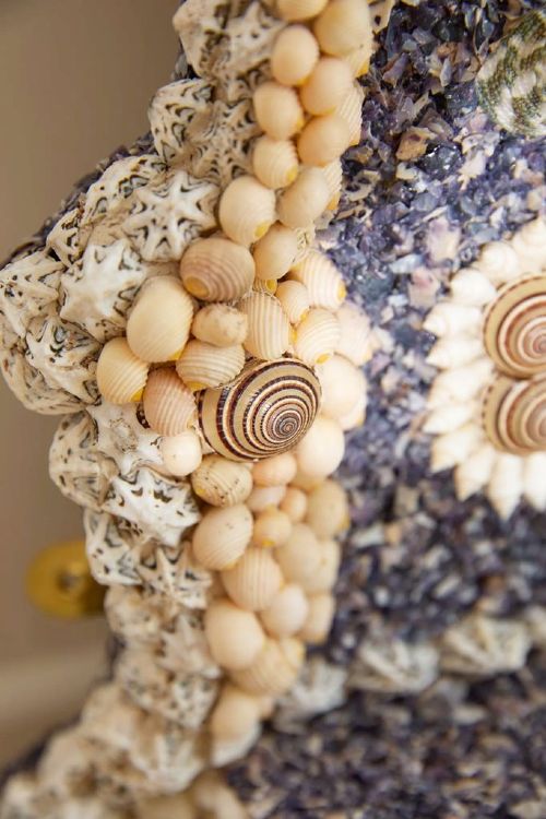 An architectural Georgian wall mirror frame encrusted with natural cream shells and dark blue mineral accents surrounding a central oval glass plate. View III
