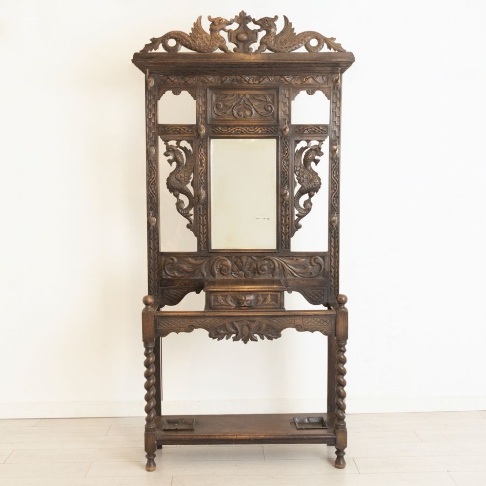 A late Victorian carved dark oak hall stand featuring a central mirror, dragon motifs, barley twist supports, integrated coat hooks, and an umbrella stand base. View II