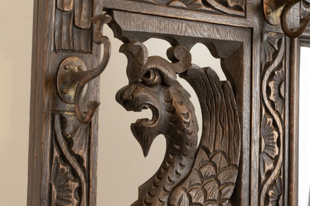 A late Victorian carved dark oak hall stand featuring a central mirror, dragon motifs, barley twist supports, integrated coat hooks, and an umbrella stand base. View III