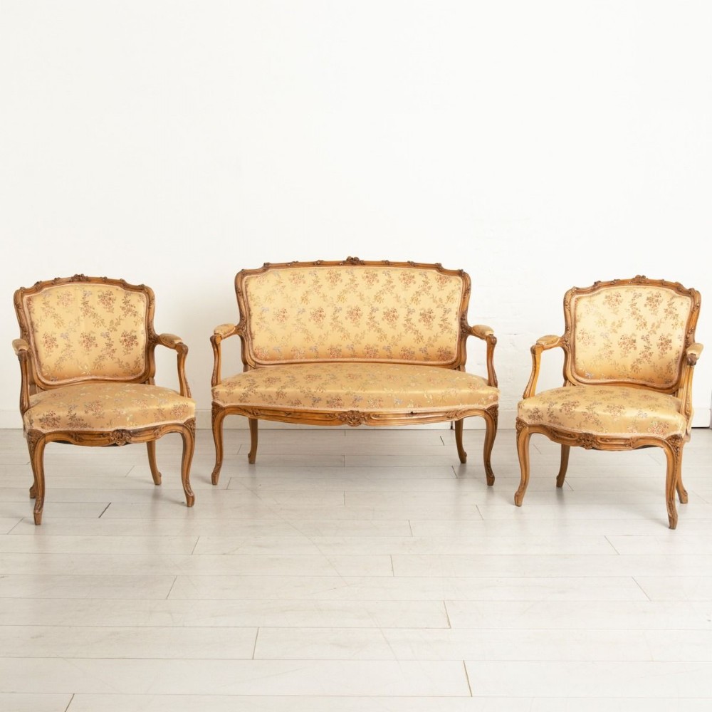 A three-piece antique French salon suite comprising a small canape sofa and two matching armchairs with carved pale walnut frames and gold floral upholstery.