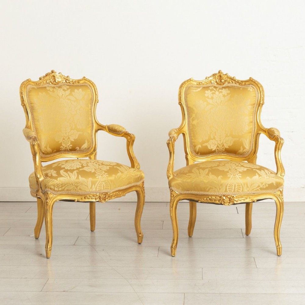 A pair of carved French Rococo giltwood armchairs upholstered in yellow silk floral damask fabric.