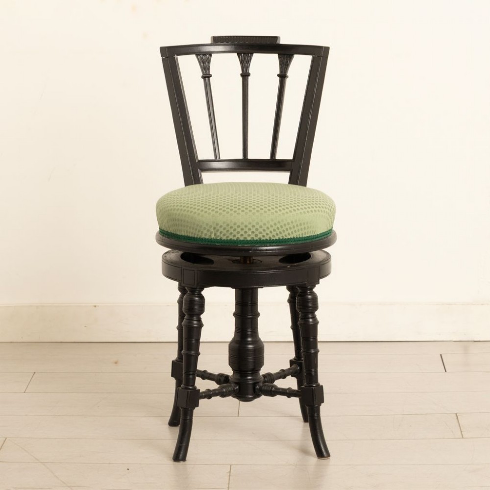 An ebonised wooden swivel piano stool featuring a spindled backrest, turned legs, and a round green upholstered seat.