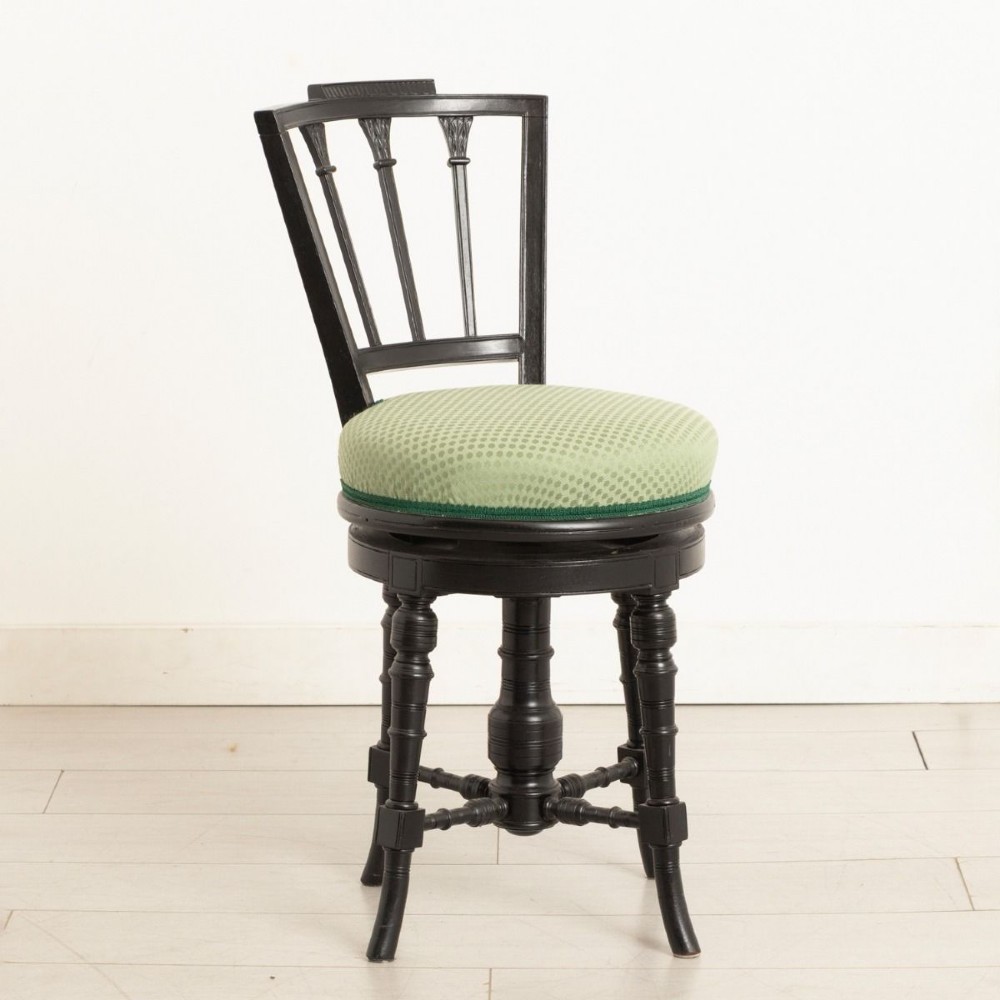 An ebonised wooden swivel piano stool featuring a spindled backrest, turned legs, and a round green upholstered seat. View II