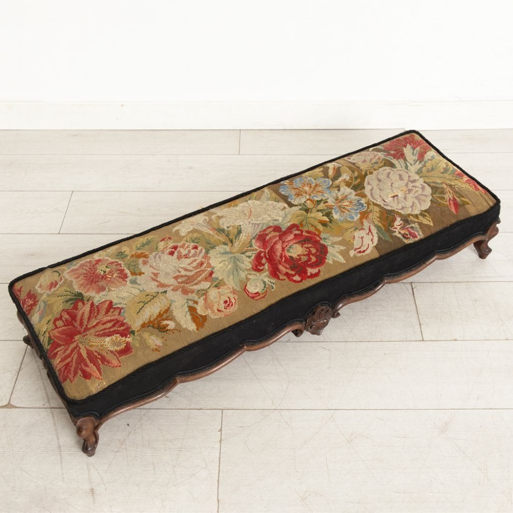 A low rectangular Victorian footstool crafted from carved dark walnut with short cabriole legs and floral tapestry upholstery. View II