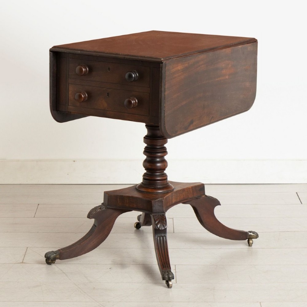 A Regency mahogany Pembroke table featuring two drawers with turned knobs, a central pedestal column, and four reeded sabre legs with brass castors.