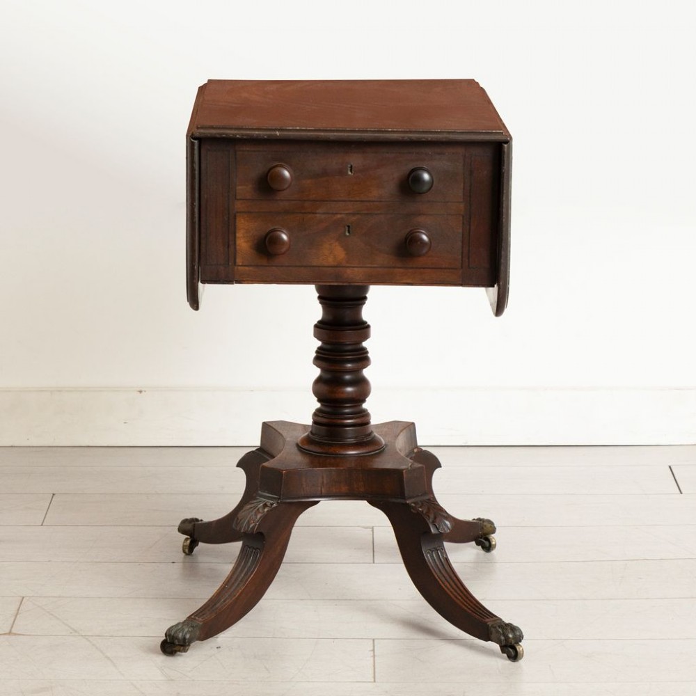 A Regency mahogany Pembroke table featuring two drawers with turned knobs, a central pedestal column, and four reeded sabre legs with brass castors. View II