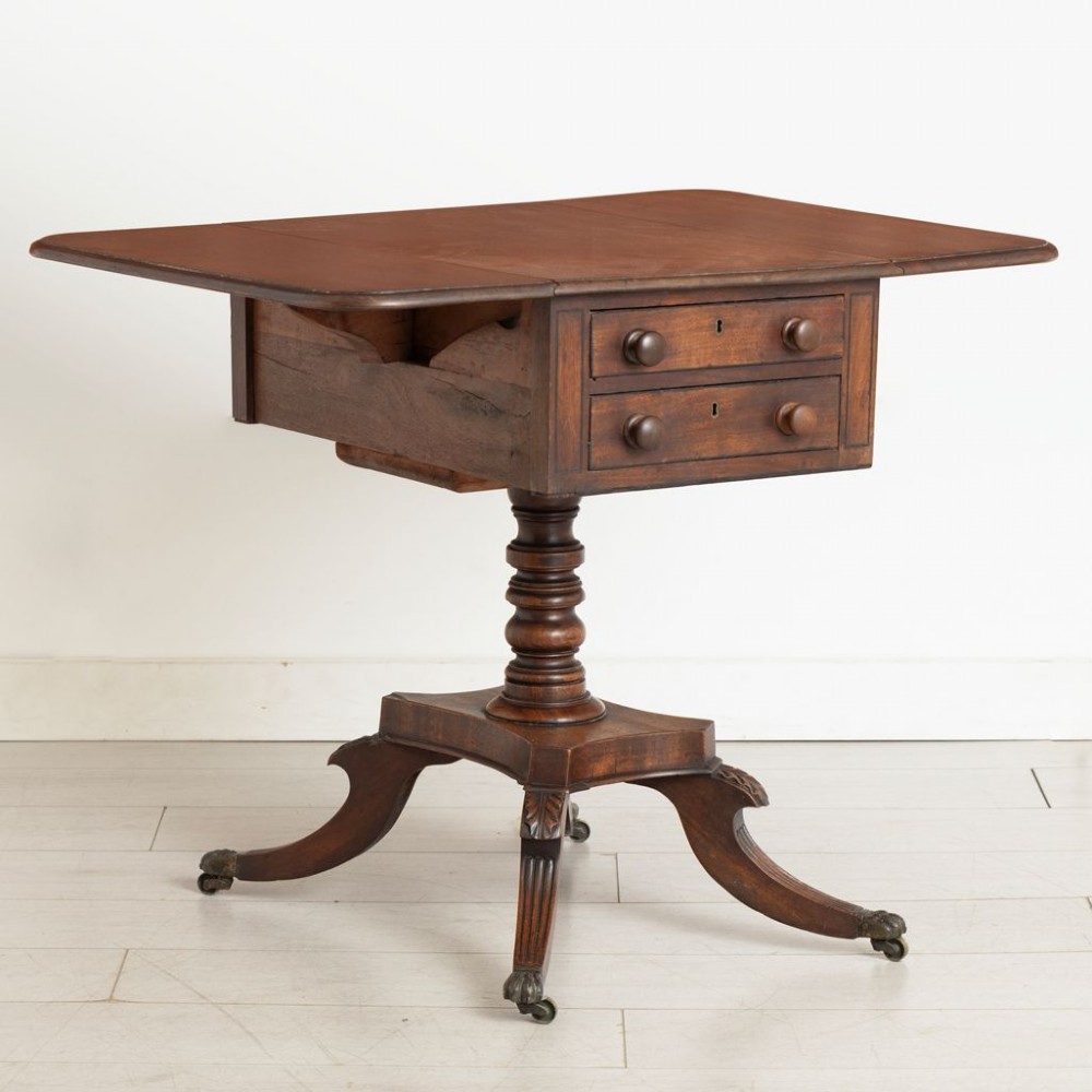 A Regency mahogany Pembroke table featuring two drawers with turned knobs, a central pedestal column, and four reeded sabre legs with brass castors. View III