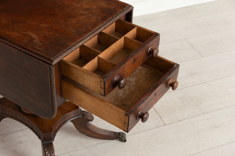 A Regency mahogany Pembroke table featuring two drawers with turned knobs, a central pedestal column, and four reeded sabre legs with brass castors. View IV