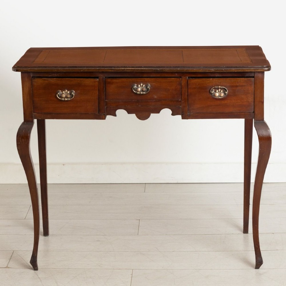 An Edwardian mahogany ladies writing desk featuring a brown leather inlaid top, three frieze drawers with brass handles, and slender cabriole legs.
