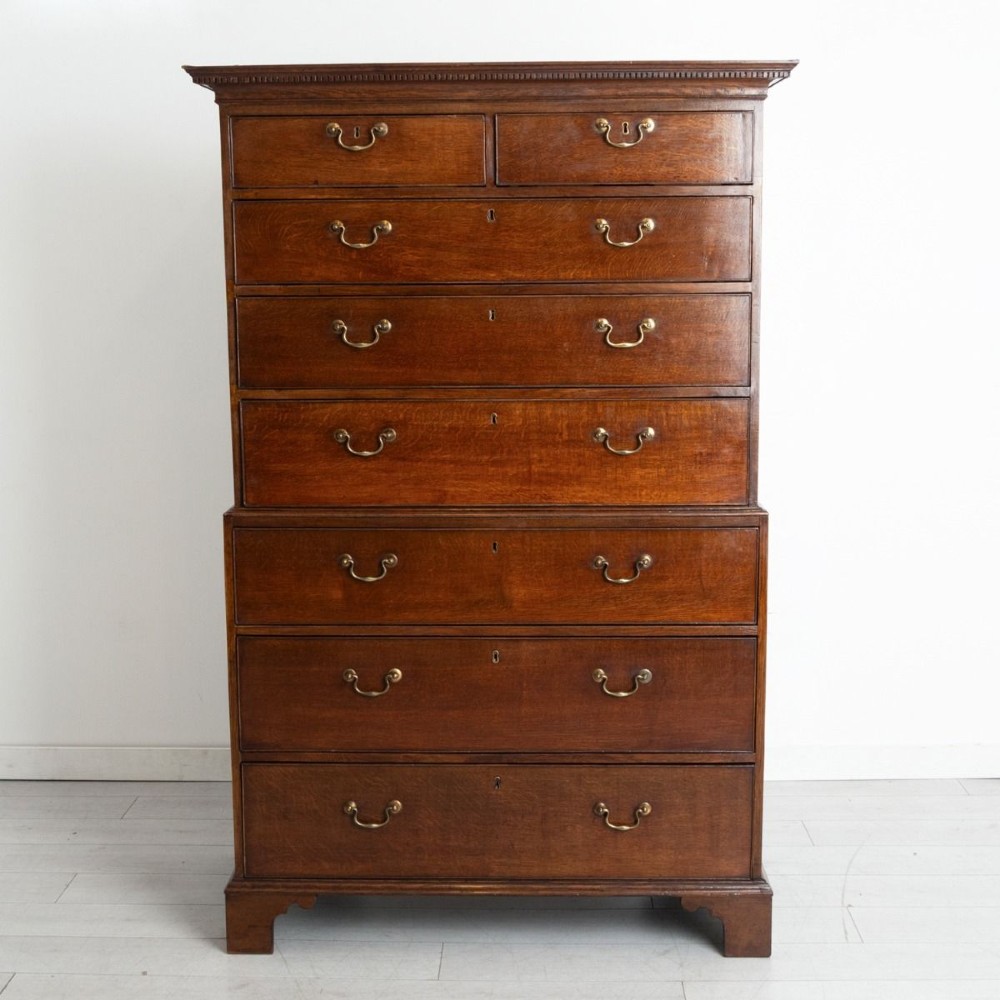 A tall Georgian oak chest on chest featuring two short drawers over five graduated long drawers with brass swan-neck handles and bracket feet.