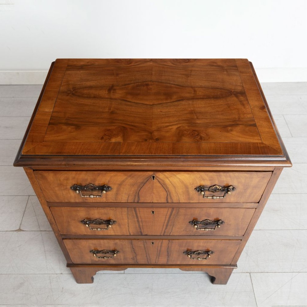 A small antique warm brown walnut chest of drawers featuring three drawers with decorative brass handles and shaped bracket feet. View II
